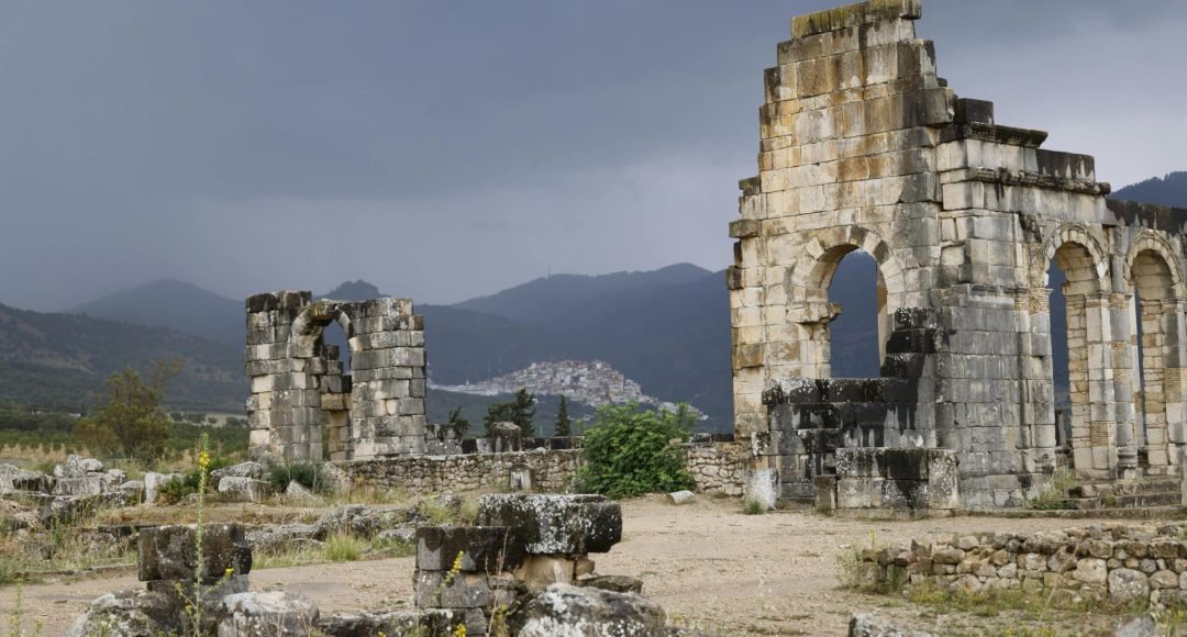Explore the ancient Roman ruins of Volubilis, Morocco, amidst a dramatic landscape.
