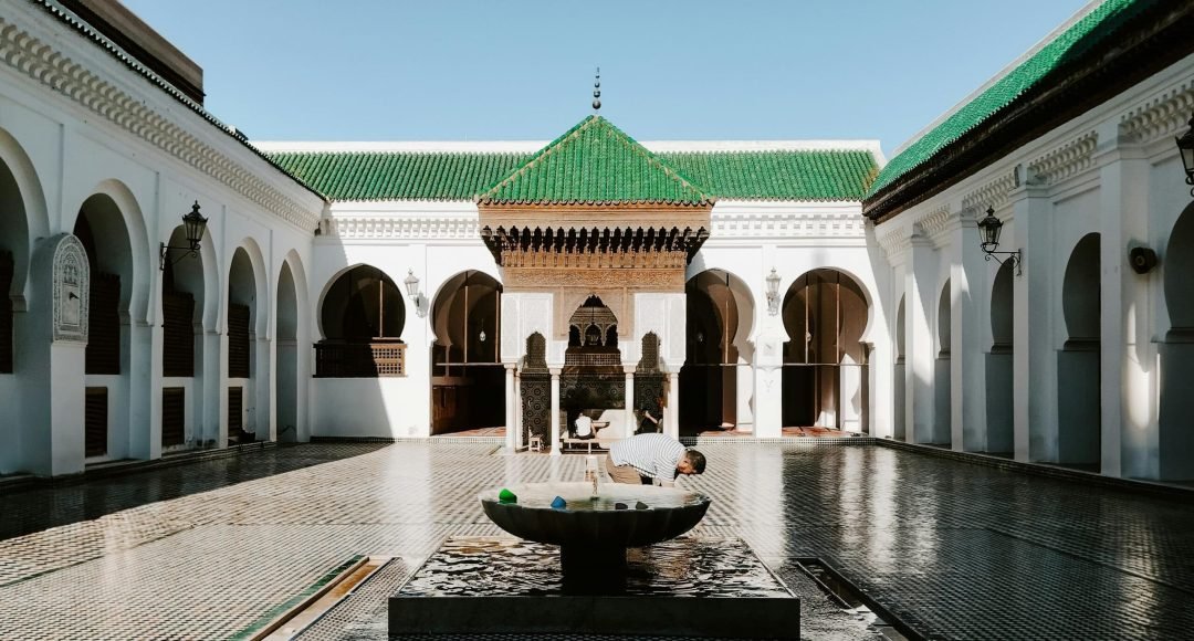 A view of the historic Al Quaraouiyine Mosque courtyard in Fes, Morocco with traditional architecture and ornate fountain.