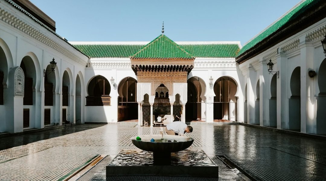 A view of the historic Al Quaraouiyine Mosque courtyard in Fes, Morocco with traditional architecture and ornate fountain.
