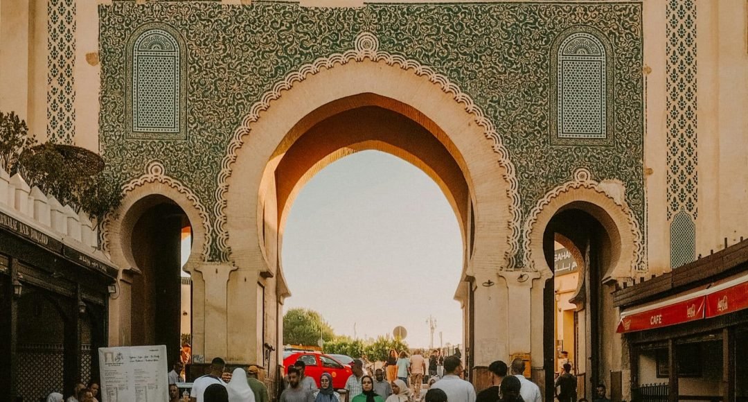 People walking through the historic Blue Gate in Fes Medina, Morocco, showcasing vibrant Moroccan architecture.